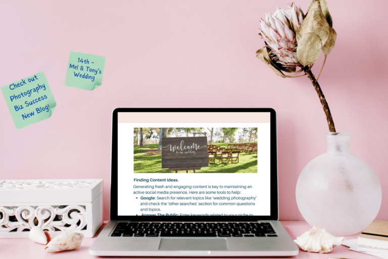 A laptop on a desk with post-it notes on a well and a flower in a vase.