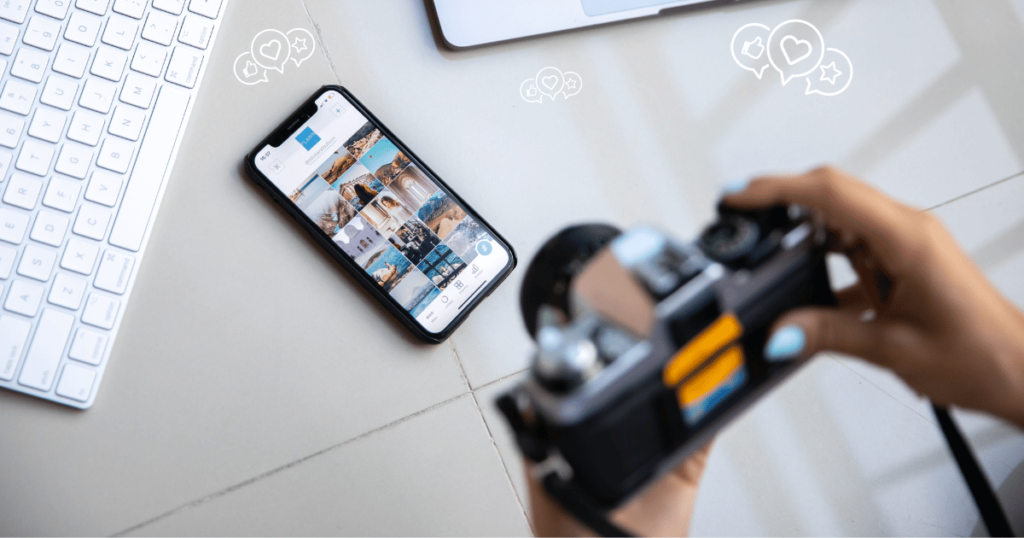 This image is of a photographer holding their camera above a desk with a mobile phone on and a social media page open on it. 