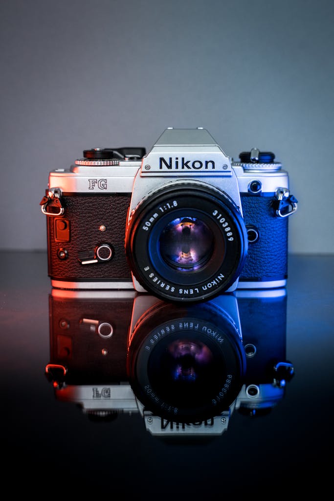 Classic Nikon film camera with lens reflecting on surface, dual lighting.