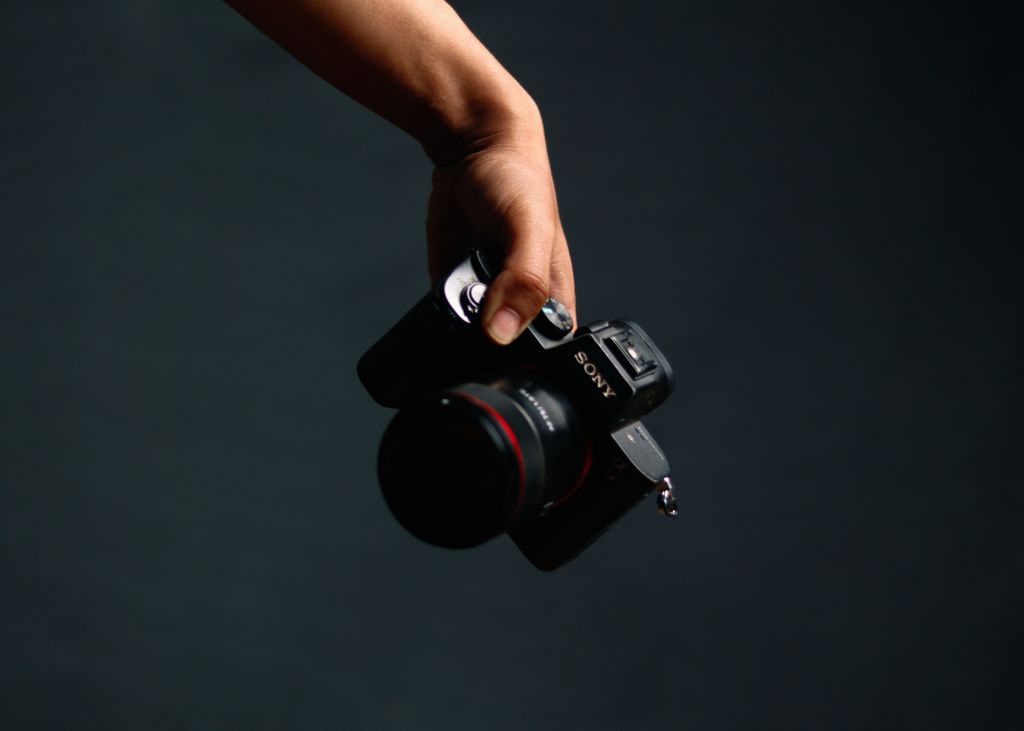 A close-up shot of a hand holding a professional camera against a dark background.